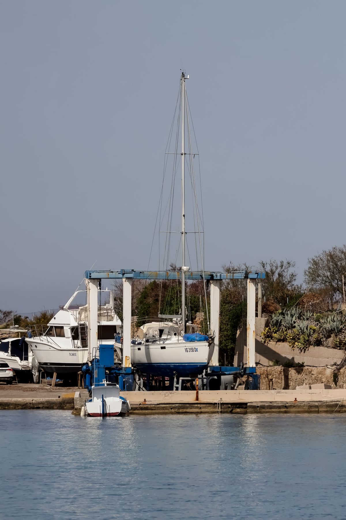 A sailboat lifted in a travel hoist at a marina for haul-out